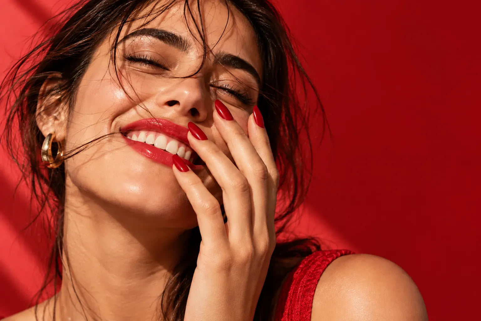 Glossy cherry-red manicure in sunlight against a coral-red backdrop
